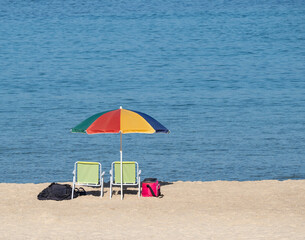 Multi-colored bright sunny umbrella, two sun loungers on the Mediterranean coast. Israel.copy space