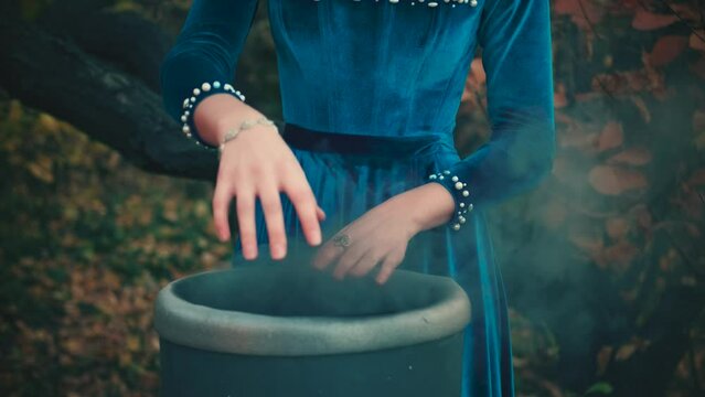 Gothic woman closeup portrait female witch hands. Lady girl magician creates magic. sorceress conjures gesture cast spell with fingers antique vat. Halloween holiday concept. Blue velvet vintage dress