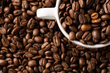 Image of white cup full of coffee beans on pile of coffee beans