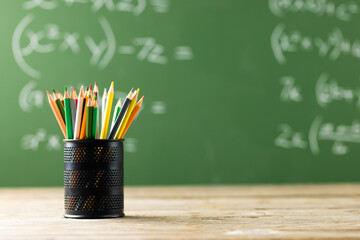 Image of cup with crayons over mathematical formulas on black board