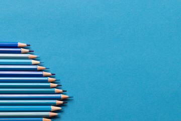Image of row of different shades of blue crayons on blue background