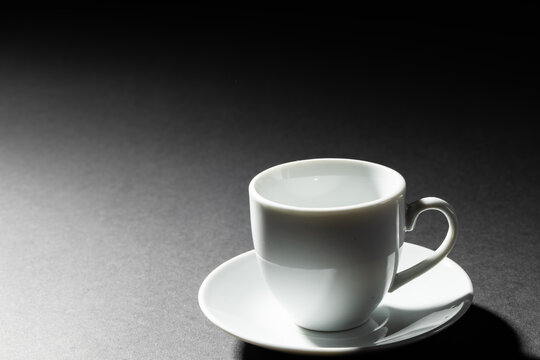 Image of empty white coffee cup and plate on black background