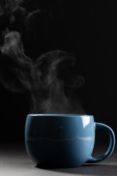 Image of blue cup of hot black coffee on black background