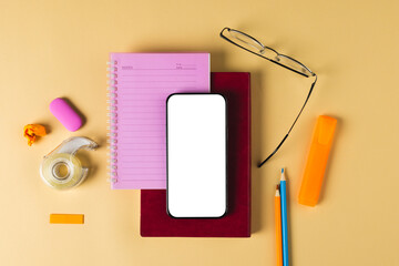 Fototapeta na wymiar Composition of smartphone with copy space, notebooks, glasses and school tools on yellow surface