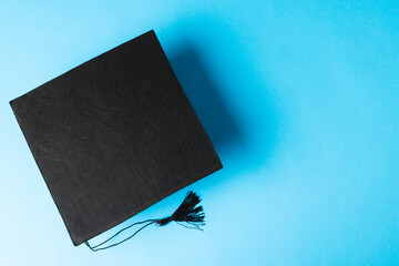 Image of black graduation hat on blue surface with copy space