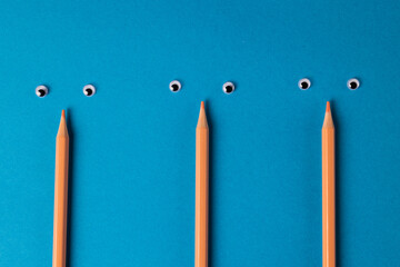 Composition of pencils with eyes on blue surface