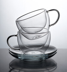 Two glasses for coffee or tea, standing on top of each other on a gray background with reflection.