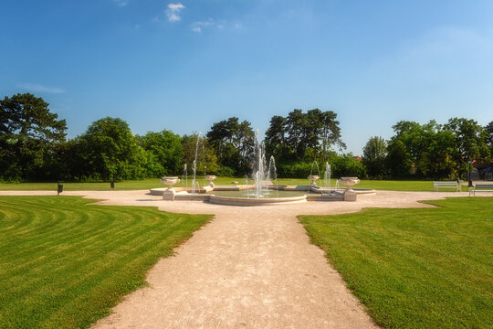 Beautiful garden of Festetics Palace with green grass and trees, decorative fountain and blue sky on a sunny summer day, Keszthely, Zala, Hungary. Outdoor travel background