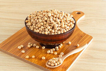 soybean in a bowl with wooden chopping board and spoon on wooden background, front view, selective focus.