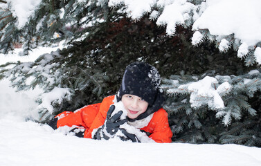 Fototapeta na wymiar a boy in an orange jumpsuit lies in the snow in winter