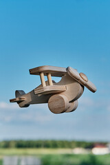 Wooden toy light aircraft biplane flying in the sky above countryside. Cartoon aviation.