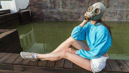 A girl in a gas mask sits by the fountain. Alienation in the city. Fashion, ecology and loneliness...