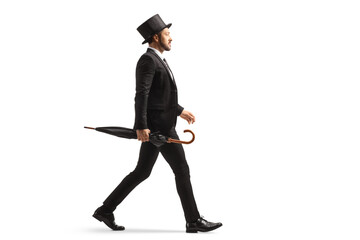 Full length profile shot of a man in a suit and top hat walking and carrying an umbrella - obrazy, fototapety, plakaty
