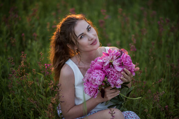 Fototapeta premium Beautiful happy young girl with peonies in nature outdoors in the sun. Beautiful woman in a field with flowers in a long skirt