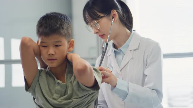 Asian female doctor examining boy with stethoscope and then showing thumb up to him during health checkup in clinic
