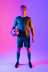 Portrait of caucasian male soccer player with football over neon pink lighting