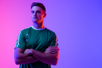 Portrait of caucasian male soccer player with arms crossed over neon pink lighting