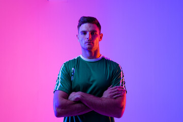 Portrait of caucasian male soccer player with arms crossed over neon pink lighting