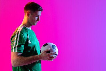Caucasian male soccer player with football over neon pink lighting
