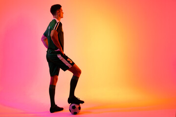 Fototapeta na wymiar Caucasian male soccer player with football over neon pink lighting