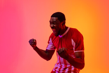Happy african american male soccer player raising hands over neon pink lighting © vectorfusionart
