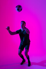 Caucasian male soccer player playing with football over neon pink lighting