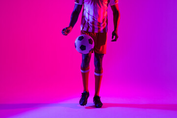 Fototapeta na wymiar African american male soccer player with football over neon pink lighting