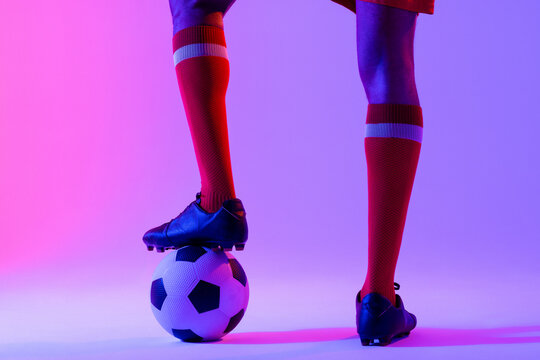 African american male soccer player with football over neon pink lighting