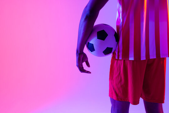 African american male soccer player with football over neon pink lighting