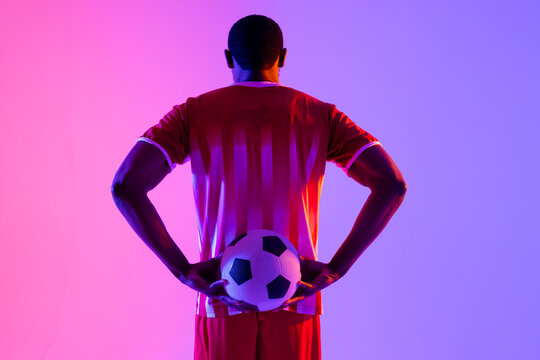 African american male soccer player with football over neon pink lighting