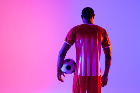 African american male soccer player with football over neon pink lighting