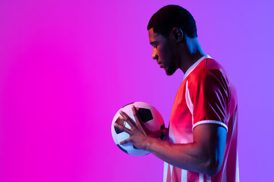 African american male soccer player with football over neon pink lighting