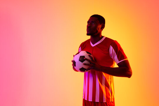 African american male soccer player with football over neon pink lighting