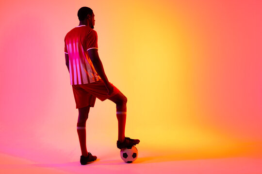 African american male soccer player with football over neon pink lighting