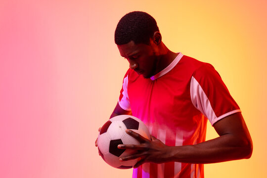 African american male soccer player with football over neon pink lighting