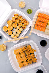 Set of fish sushi rolls with salmon and sesame,ginger,wasabi,soy sauce packed in plastic disposable container box on gray background.Seafood,Food delivery,take out service from restaurant concept