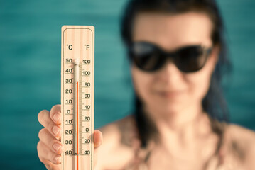 Beautiful young woman in sunglasses with a thermometer in her hand on the background of the sea. Summer vacation and heat concept, selective focus