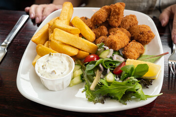 Shallow focus on scampi and chips with salad and a tub of tartare sauce. All served on a white...