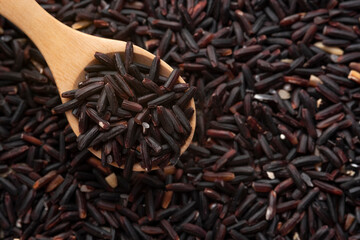 Uncooked riceberry rice on wooden spoon with copy space.Top view