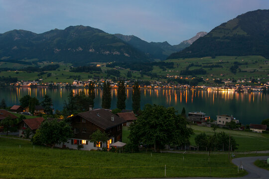 Picturesque evening landscape on Lake Sarnen in central Switzerland with mountains in the background. Evening lights in the houses are reflected in the lake.