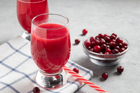 Two glass with homemade freshly cranberry juice and a bowl of cranberries on a gray concrete table