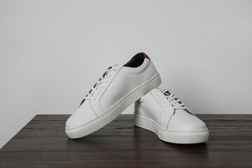 Pair of stylish white sneakers on wooden table against light background