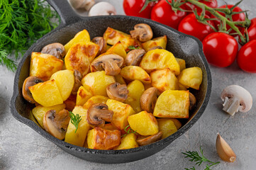 Baked potatoes with mushrooms and garlic in a cast iron skillet on a gray concrete background. Top view. Copy space.