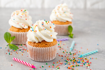 Delicious vanilla cupcakes with cream cheese and sugar candy on a gray background. Dessert for birthday. selective focus, copy space.