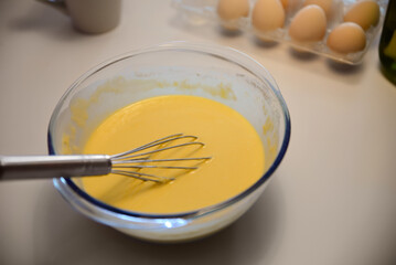 Glass bowl of crepe batter with whisk on white table, closeup