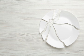 Pieces of broken ceramic plate on white wooden table, flat lay. Space for text