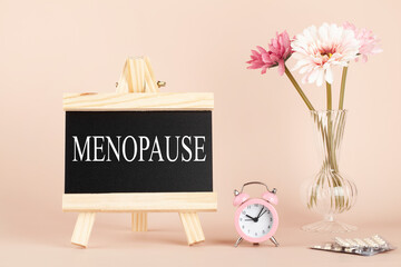 menopause word written on black board, flowers, clock and pills on beige background. women health and middle age concept. medicine, healthcare style - obrazy, fototapety, plakaty