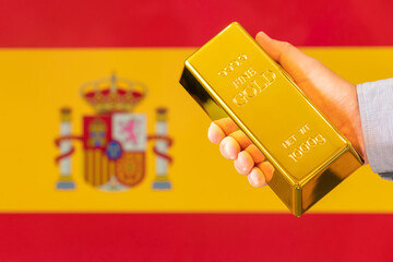 gold reserve of the Spain concept. Gold bar in hand on flag Spain background
