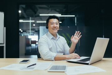 Portrait of Asian businessman man looking at camera and waving greeting gesture, man with headset for video call