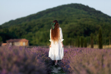 a girl with long hair decorated with a bow walks through a field of lavender